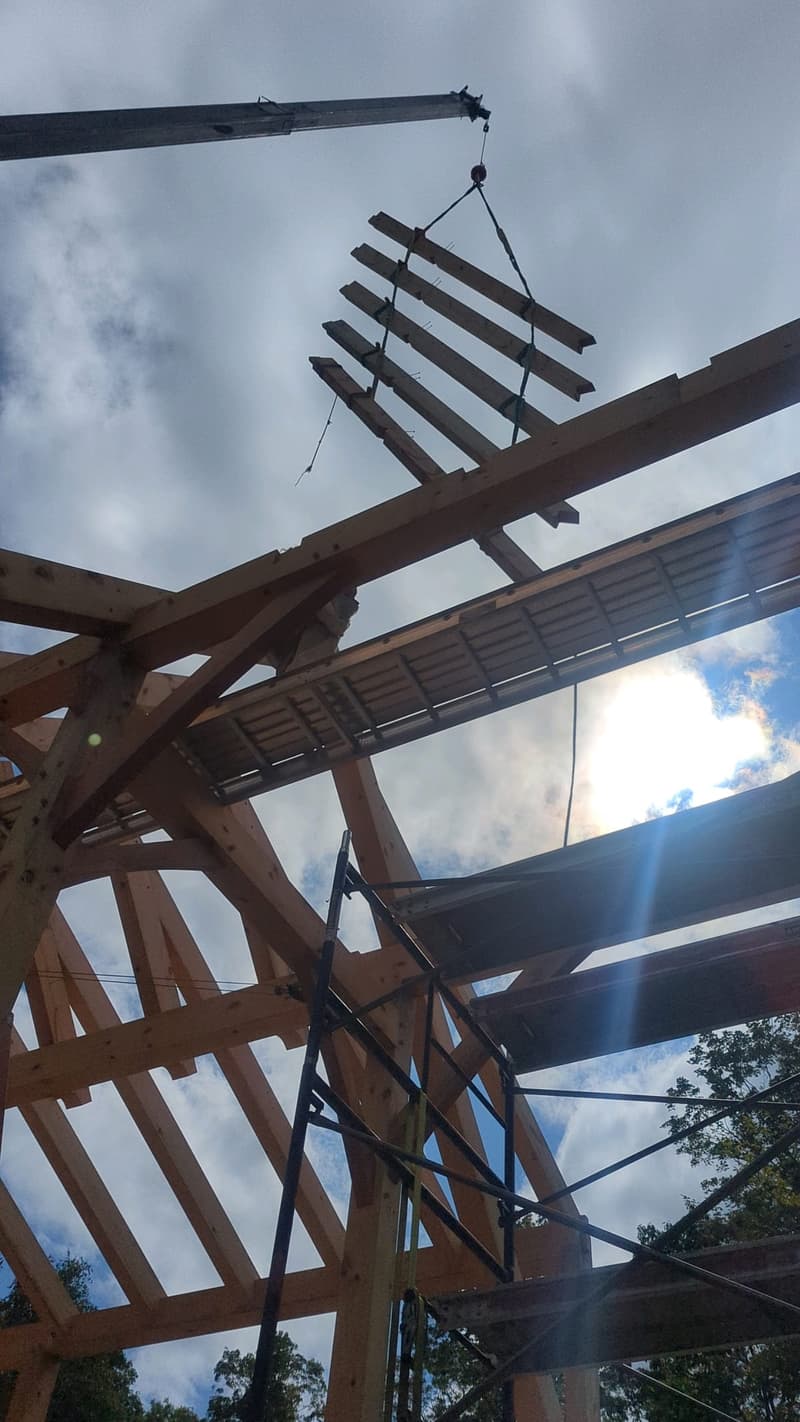 Crane lowering a timber rafter bundle onto a catalog frame during raising day