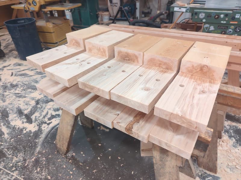 Hand-cut timber connectors lined up on sawhorses, identical layout for a catalog frame family