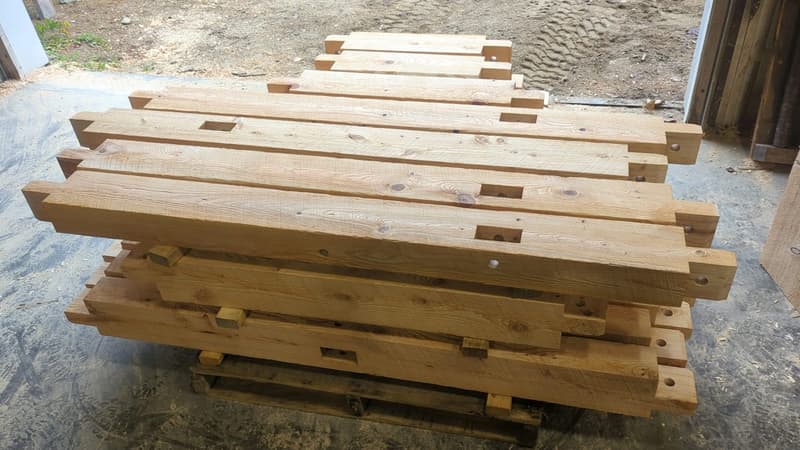 Labeled timber frame kit timbers with mortise-and-tenon joinery stacked on a pallet at the NETF shop